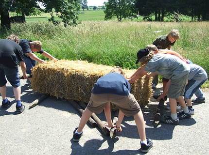 Den schweren Strohballen auf Rundhölzern fortbewegen.